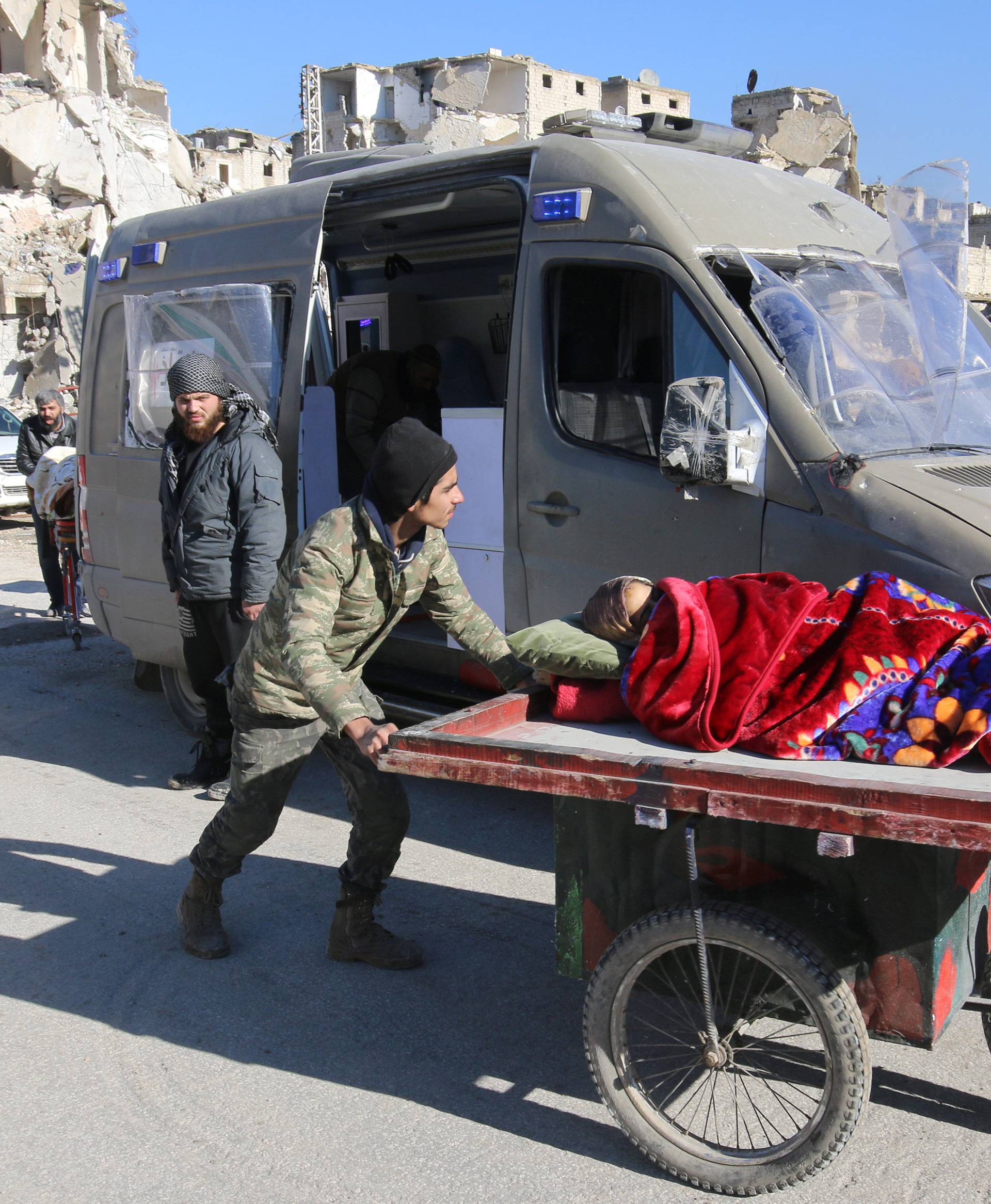 A man pushes a cart with a woman lying on it as vehicles wait to evacuate people from a rebel-held sector of eastern Aleppo