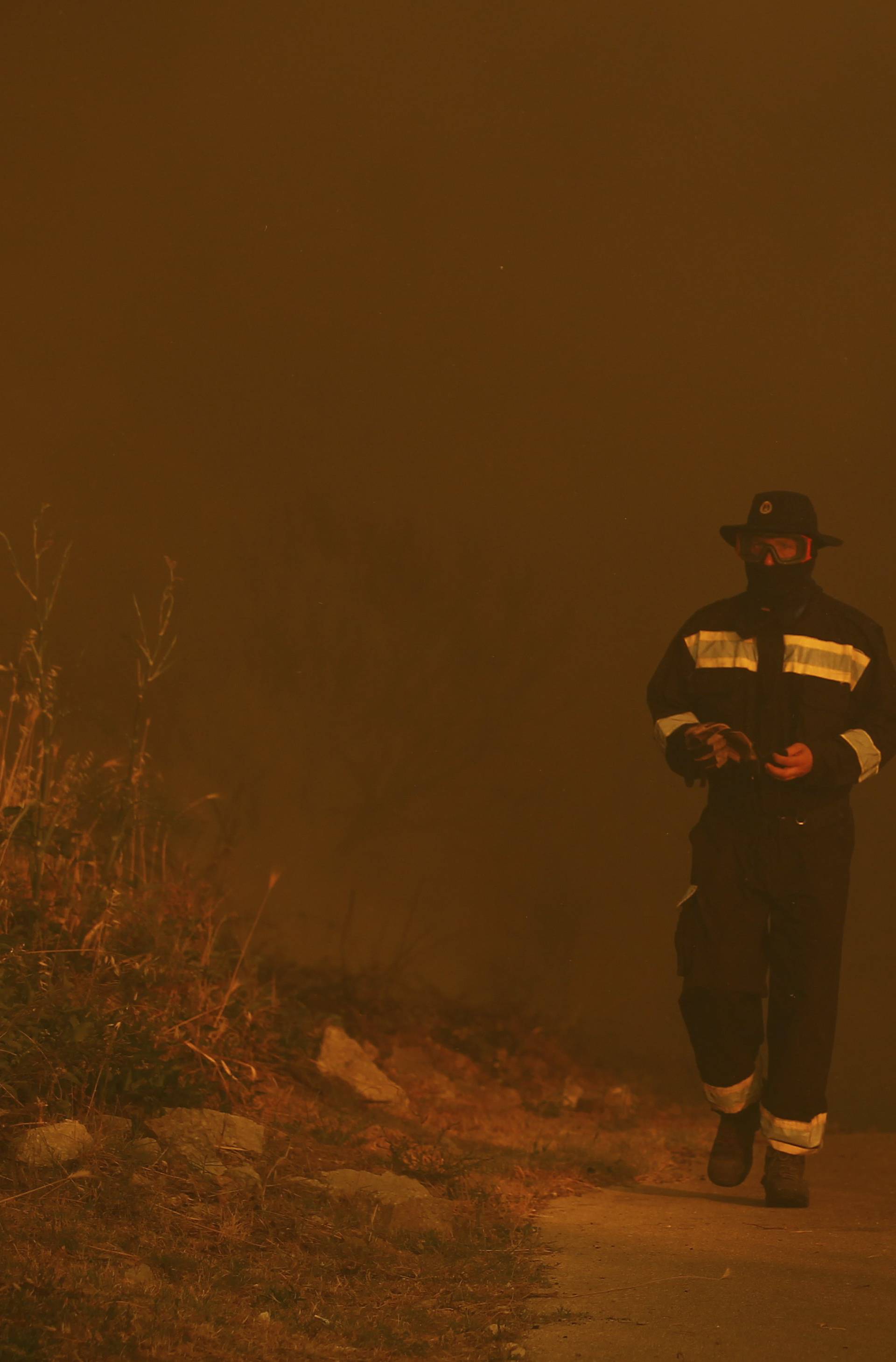 A firefighter walks amid smoke after trying to extinguish a wildfire in the village of Mravince