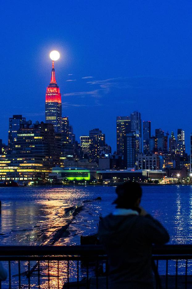 The Supermoon rises behind the Empire State Building while it glows red in solidarity with those infected with coronavirus as the outbreak of the disease (COVID-19) continues in the Manhattan borough of New York City, as it is seen from Hoboken