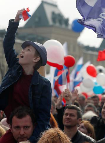 A boy sits on a man's shoulders as they attend a May Day rally in central Moscow