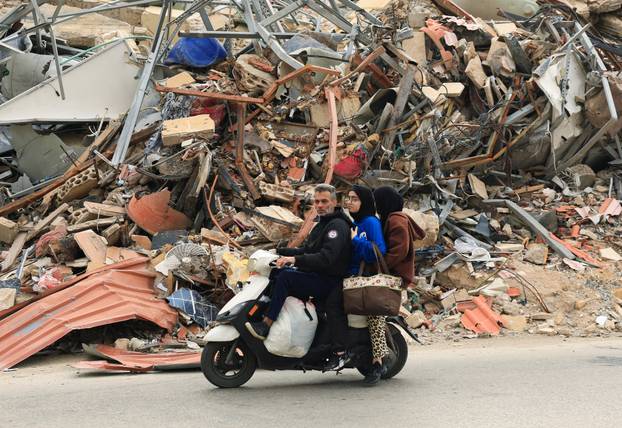 People ride past a damaged building, after a 10-day ceasefire between Lebanon and Israel went into effect, in the southern suburbs of Beirut