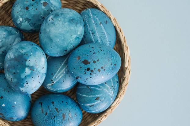 Stylish trending Easter eggs in blue tones in a wicker basket close-up on a light blue background with a place for text. Minimalistic easter background concept