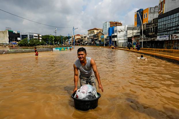 Man carries his belongings across floodwaters at the Jatinegara area after heavy rains in Jakarta