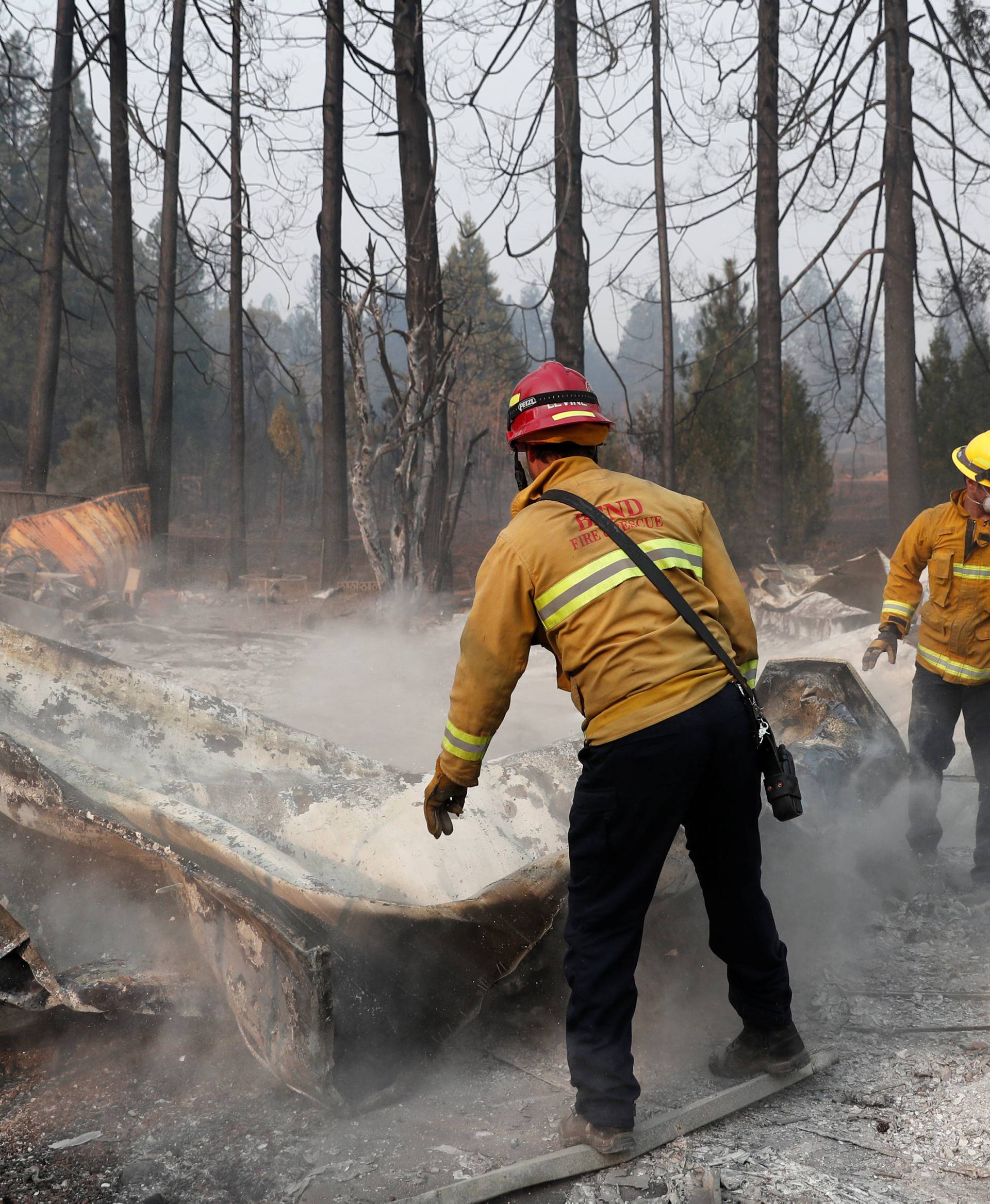 Firefighters move debris while recovering human remains from a trailer home destroyed by the Camp Fire in Paradise