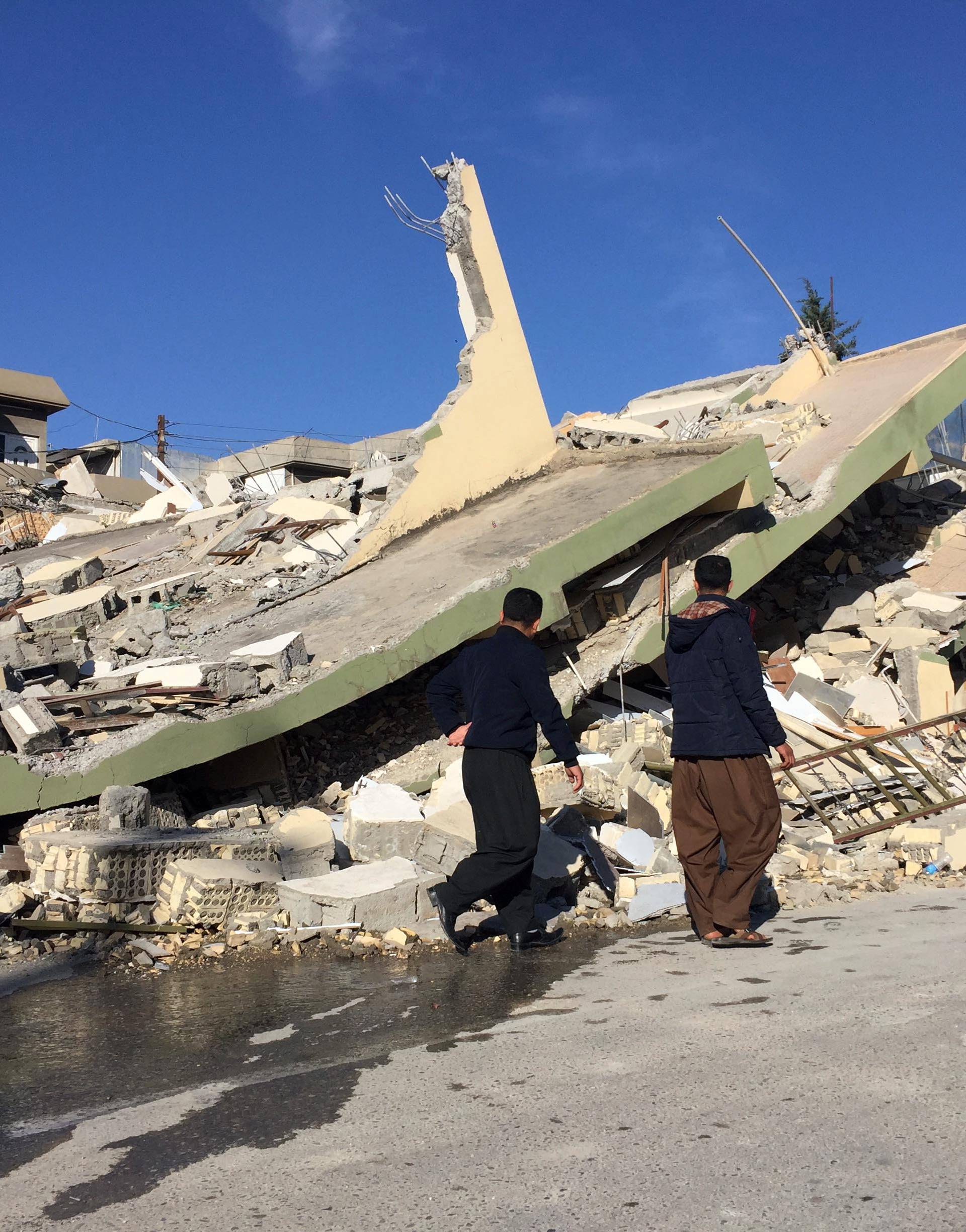 People walk past a damaged building following an earthquake in Darbandikhan