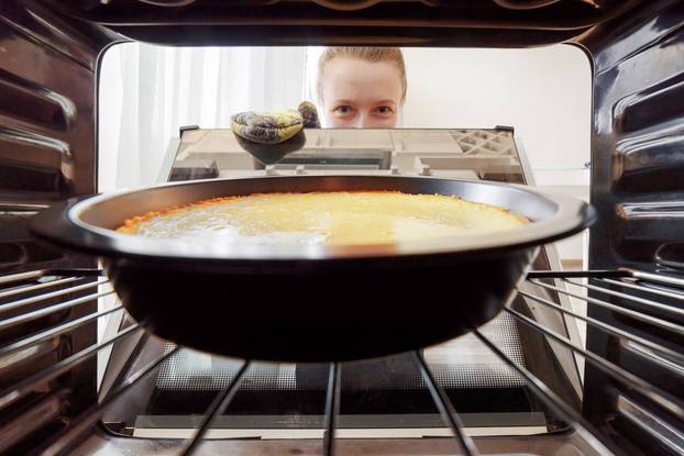 Young,Housewife,Looking,At,Cheesecake,Into,Oven,In,Kitchen.,View