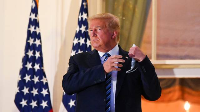 U.S. President Donald Trump pulls off his face mask as he returns to the White House after being hospitalized at Walter Reed Medical Center for coronavirus disease (COVID-19), in Washington