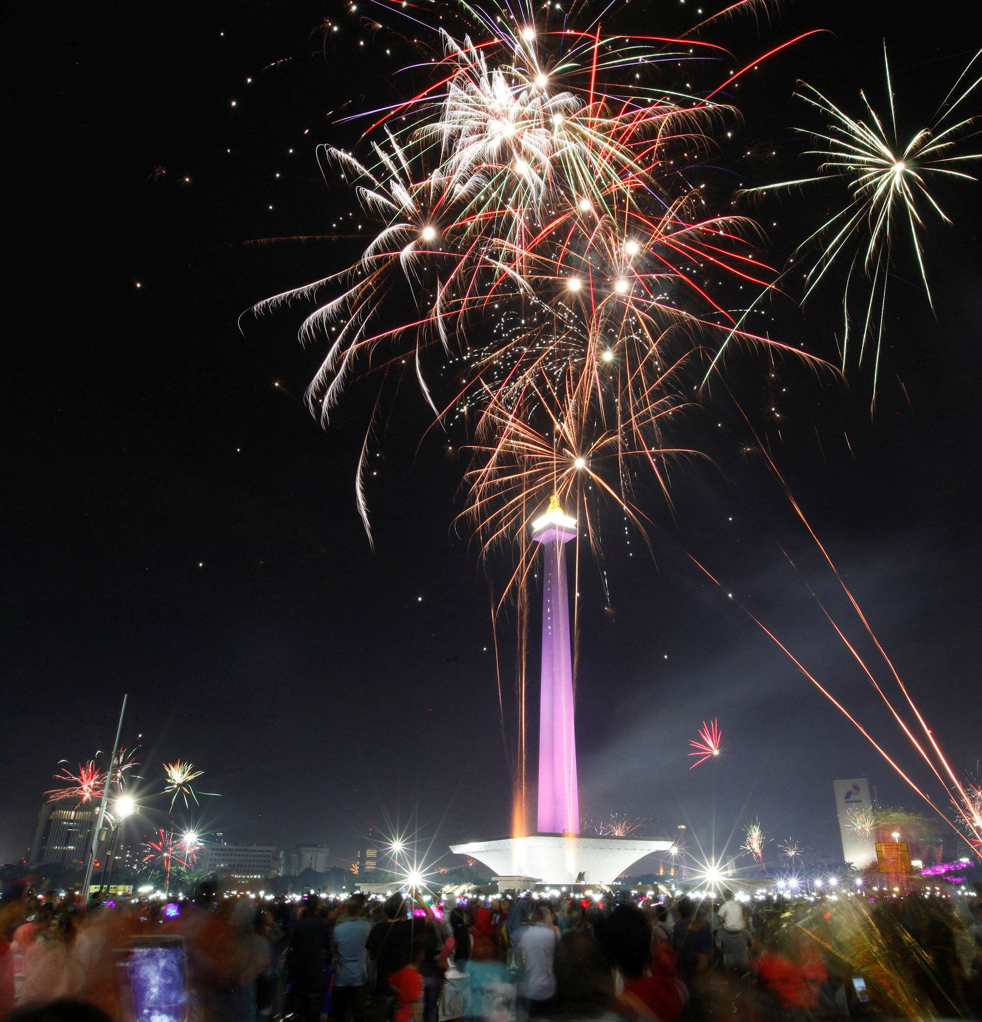 People watch fireworks explode around the National Monument during New Year's Eve celebrations in Jakarta