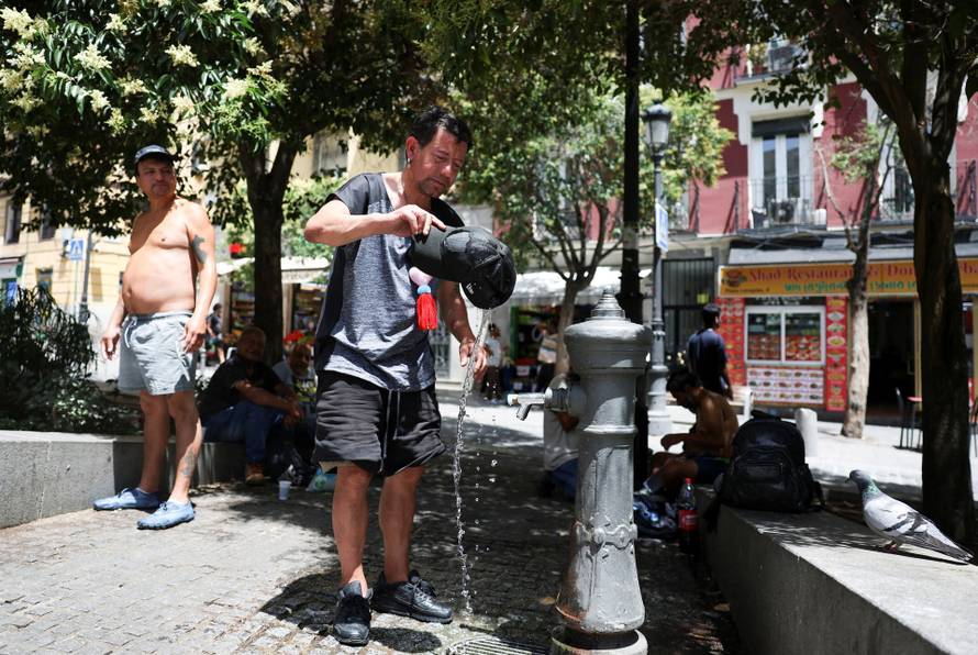 FILE PHOTO: A man rinses his hat with water to cool off during a hot day amid a heatwave in Madrid, Spain