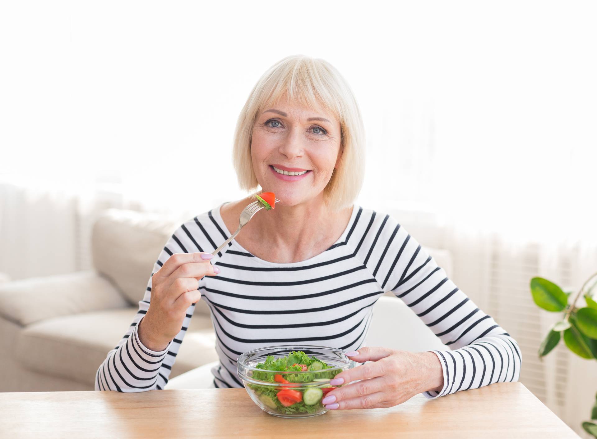 Happy senior lady eating fresh salad at home