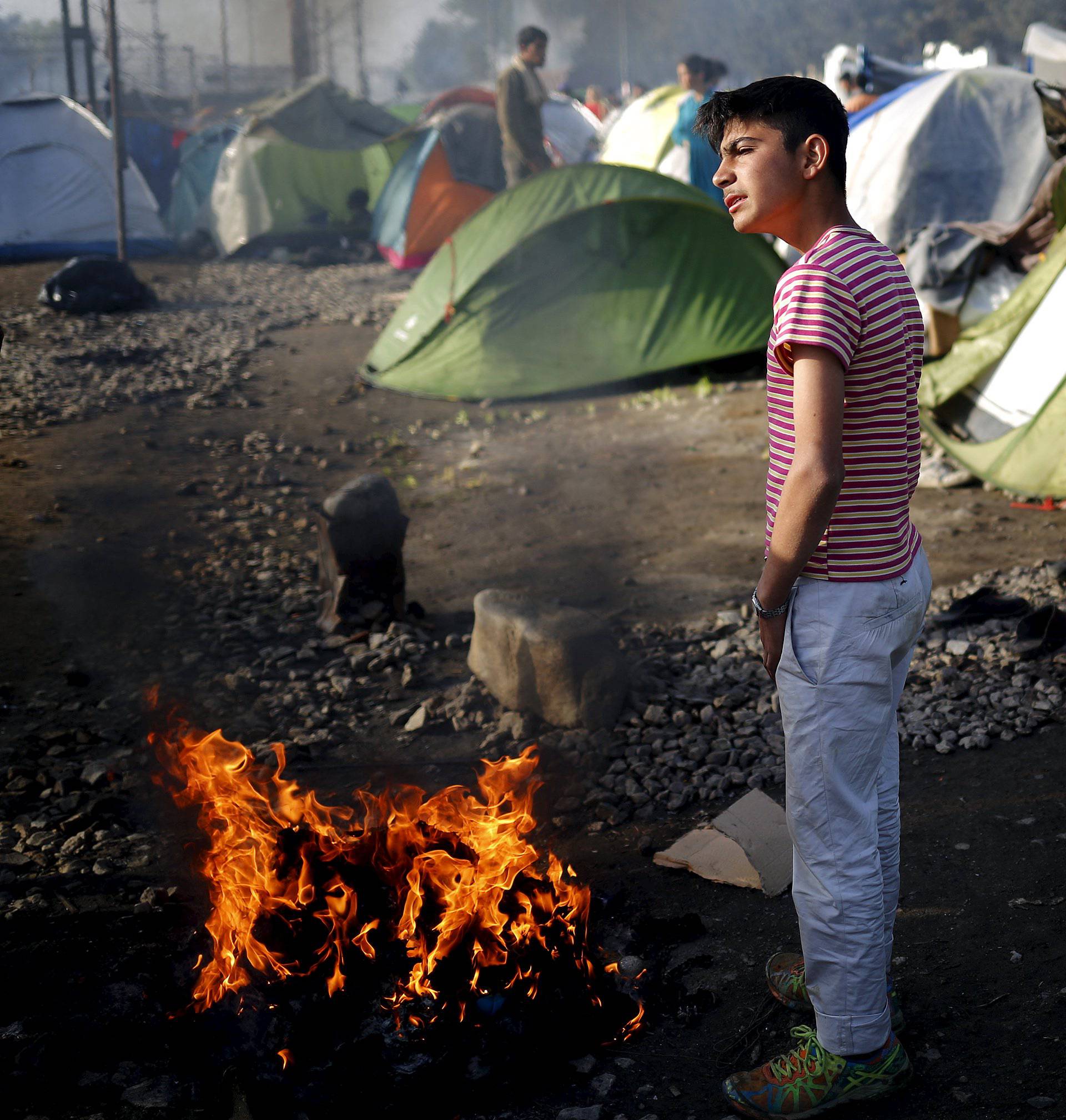 Boy warms up at a fire at a makeshift camp for migrants and refugees at the Greek-Macedonian border near the village of Idomeni