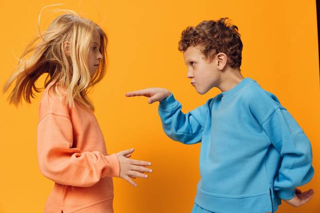 happy little children of school age stand in bright clothes on a yellow background and dance vigorously