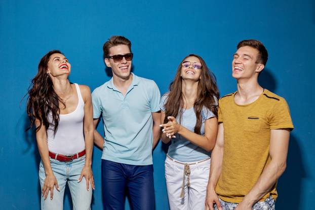Four Good-Looking Friends Are Laughing While Standing in Front of the Blue Wall. Entertainment, Having Good Time. Friendship, Relationship.