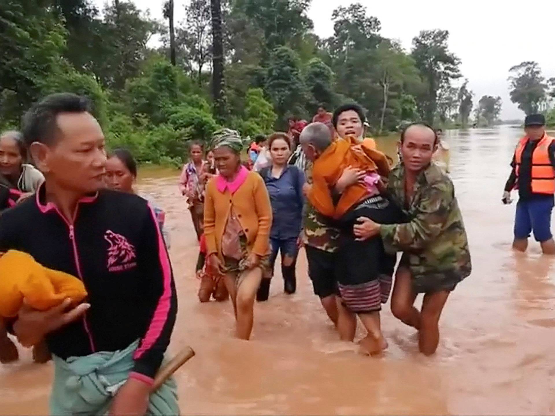 People walk through flooded area after being brought to safety by boat in Sanam Xay district, Attapeu Province, Laos after a hydropower dam under construction in Southern Laos collapsed, in this still picture taken from social media video
