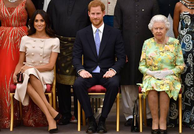 FILE PHOTO: Britain's Queen Elizabeth, Prince Harry and Meghan, the Duchess of Sussex pose for a picture with some of Queen's Young Leaders at a Buckingham Palace reception following the final Queen's Young Leaders Awards Ceremony, in London