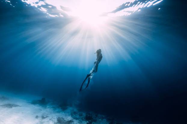 Woman freediver glides over sandy sea with fins