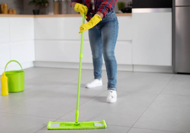 Millennial african american lady in rubber gloves with bucket and mop washes floor, enjoys household chores