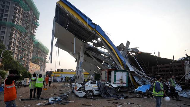 Members of rescue teams stand at a damaged fuel station after a massive billboard fell during a rainstorm in Mumbai