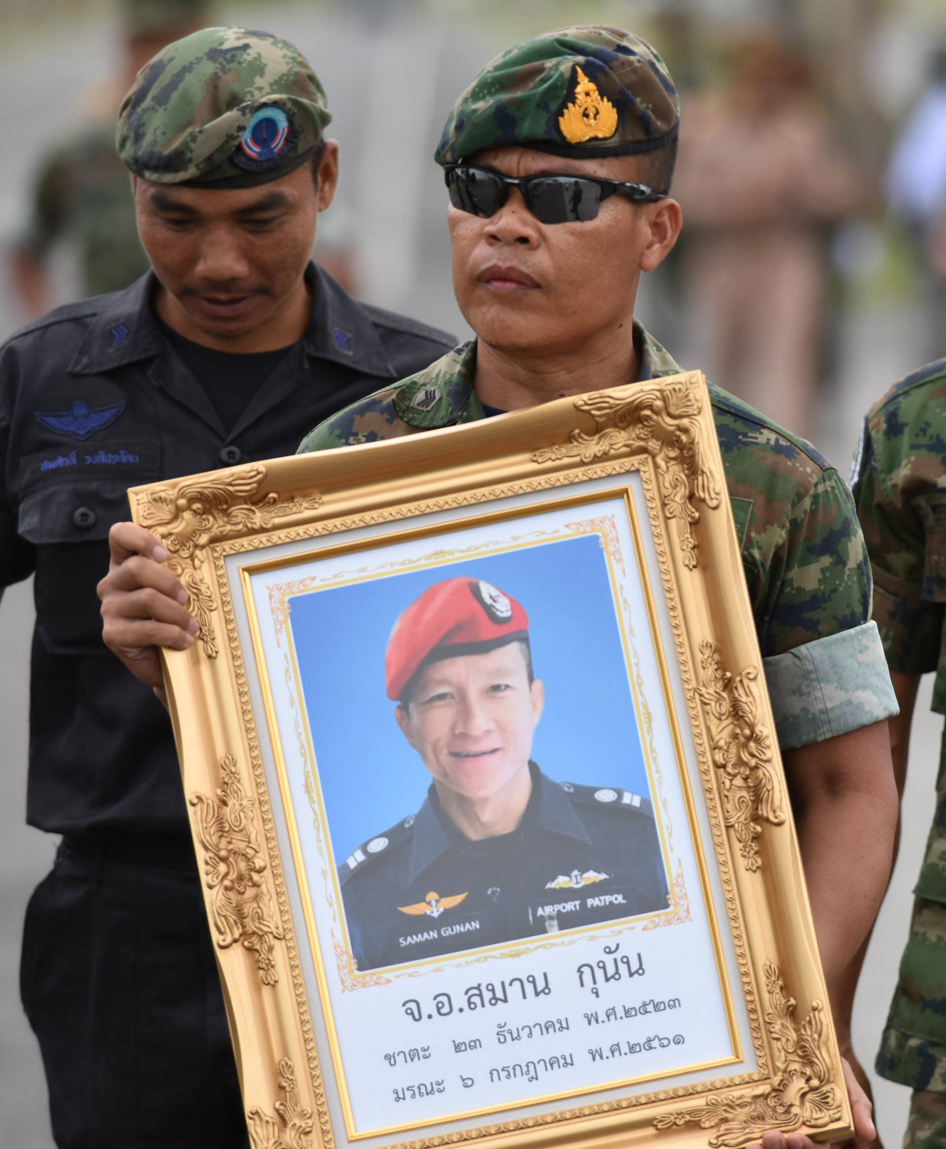 An honour guard hold up a picture of Samarn Poonan, 38, a former member of Thailand's elite navy SEAL unit who died working to save 12 boys and their soccer coach trapped inside a flooded cave as family members weep at a airport, in Rayong province