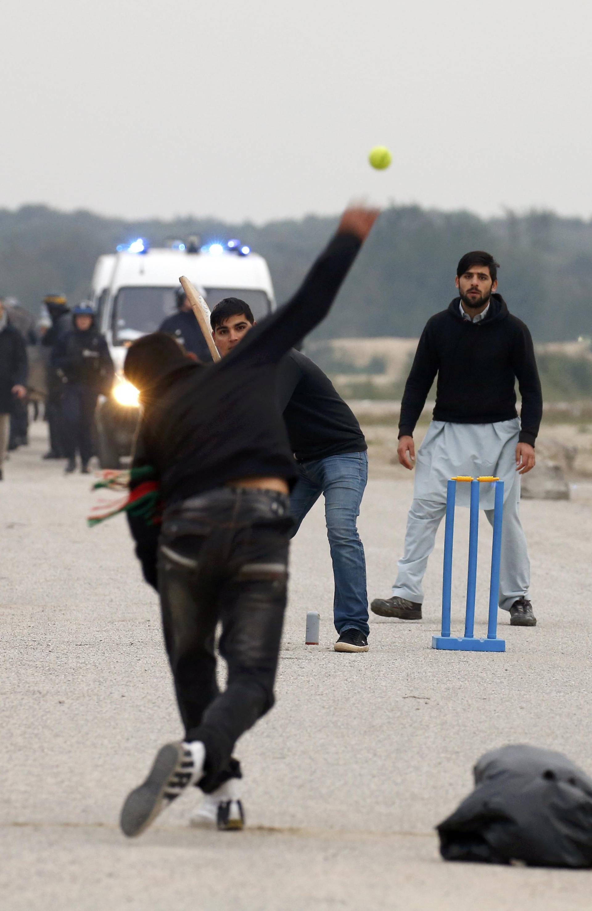 French CRS riot police secure a road as migrants play cricket on the eve of the evacuation and dismantlement of the camp called the "Jungle" in Calais