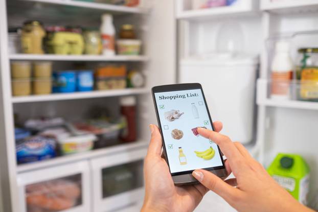 Woman makes her shopping list on his phone connected to the refr