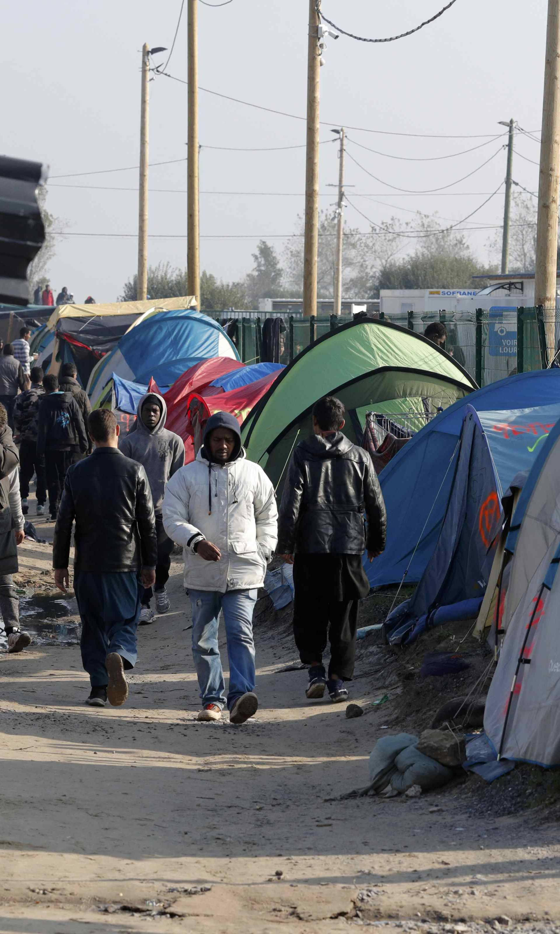 Migrants walk in an alley near tents and makeshift shelters on the eve of the evacuation and dismantlement of the camp called the "Jungle" in Calais