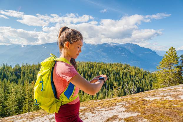Running trail runner looking sport and fitness smartwatch for training data. Runner woman running cross-country trail run training hiking outside in mountains. Squamish, British Columbia Canada