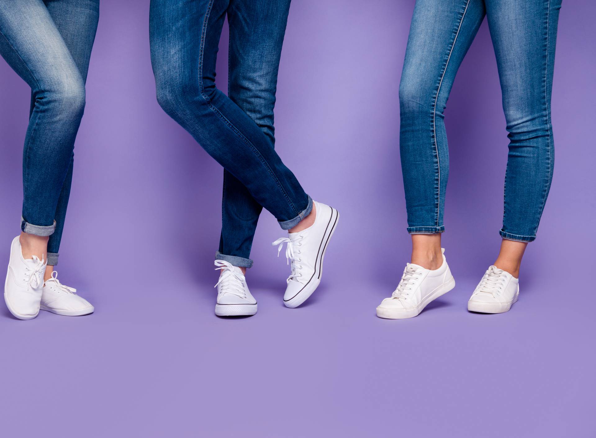Cropped closeup photo of three people's legs wearing denim dark blue jeans trousers pants standing on the floor isolated violet background