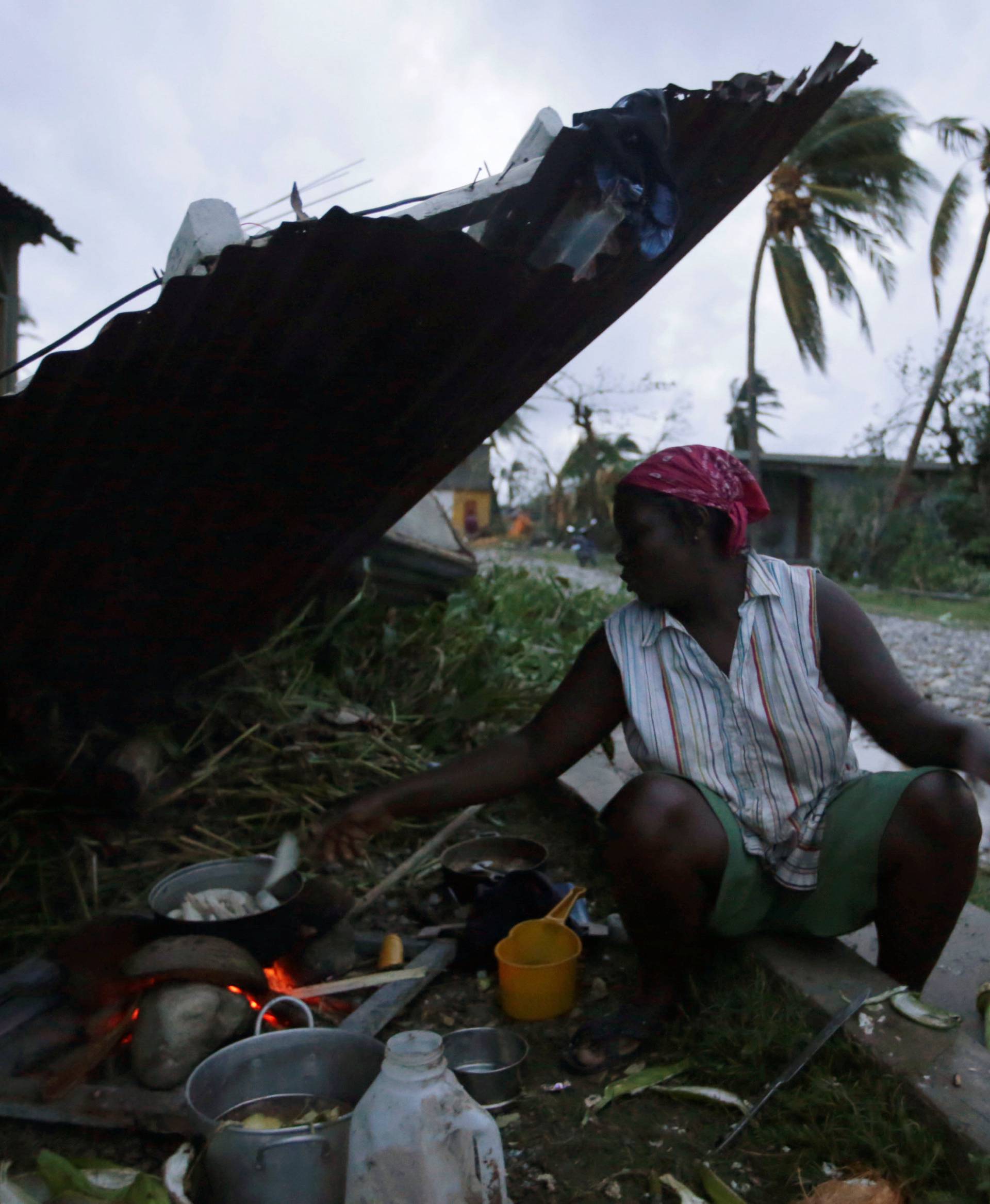 A woman cooks next to a house damaged by Hurricane Matthew in Les Cayes