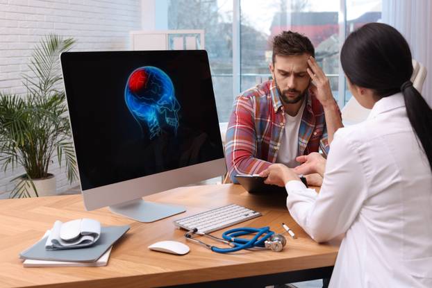 Young neurologist consulting patient at table in clinic