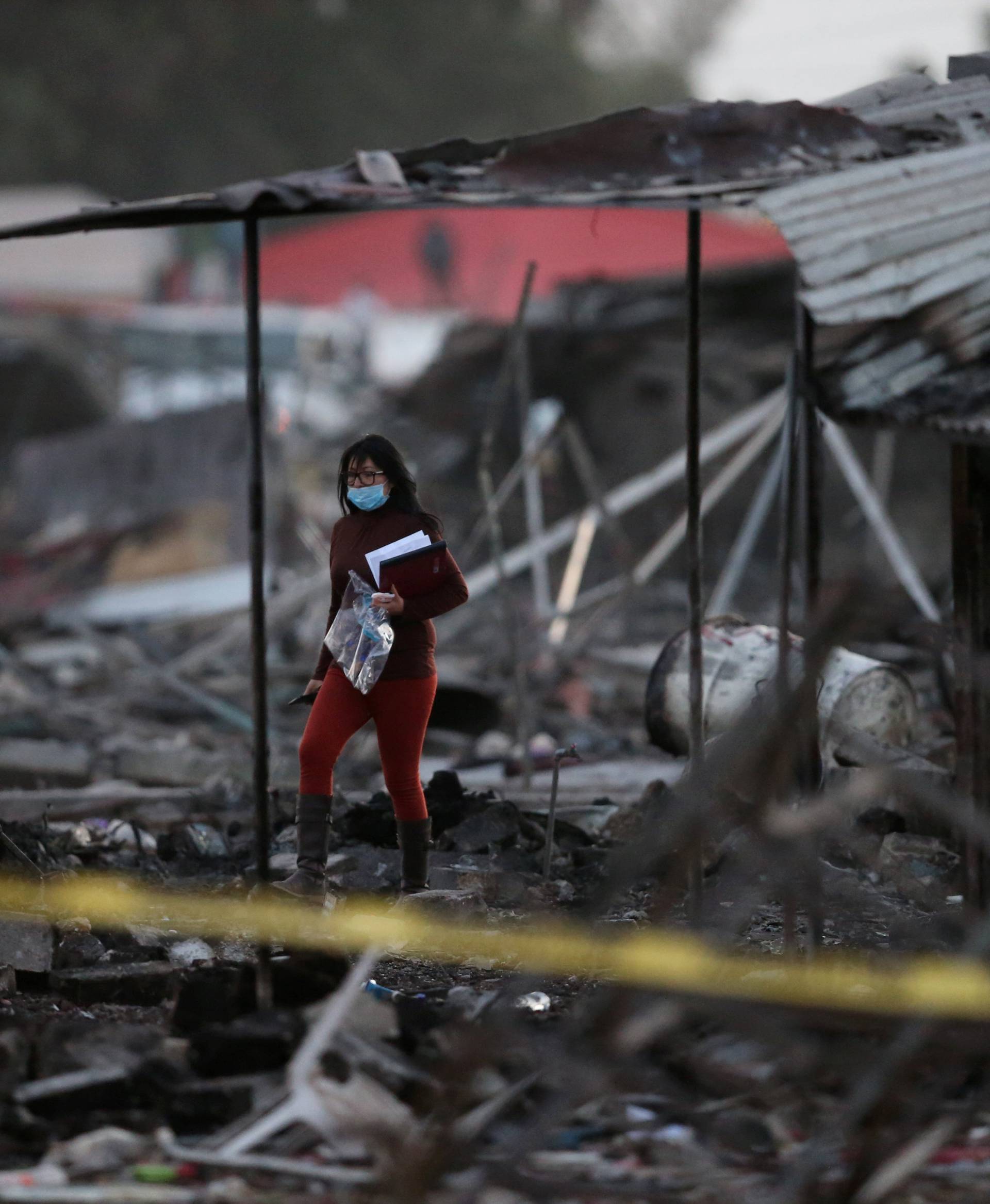 A woman walks amidst the remains of houses destroyed in an explosion at the San Pablito fireworks market in Tultepec