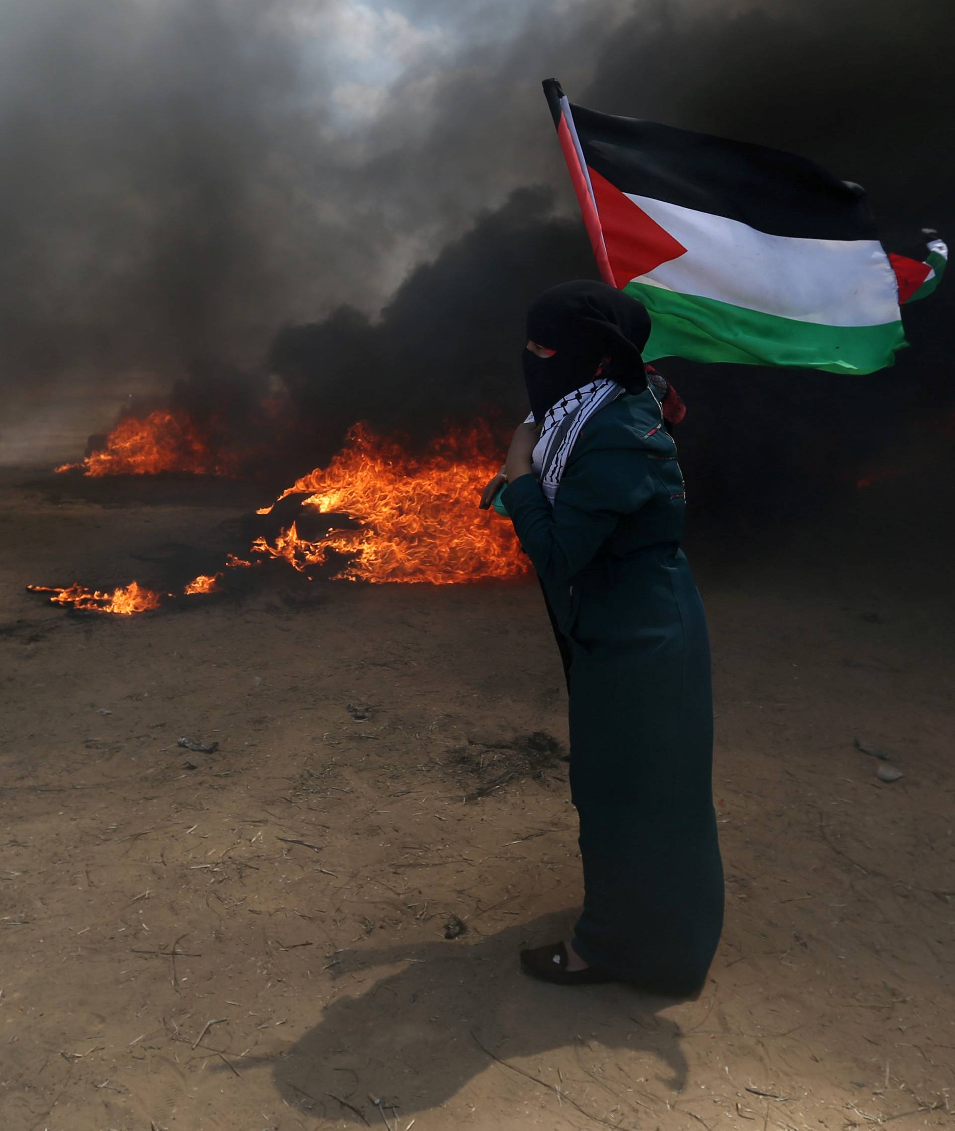 Woman holds a Palestinian flag as a demonstrator runs during a protest against U.S. embassy move to Jerusalem and ahead of the 70th anniversary of Nakba, at the Israel-Gaza border in the southern Gaza Strip