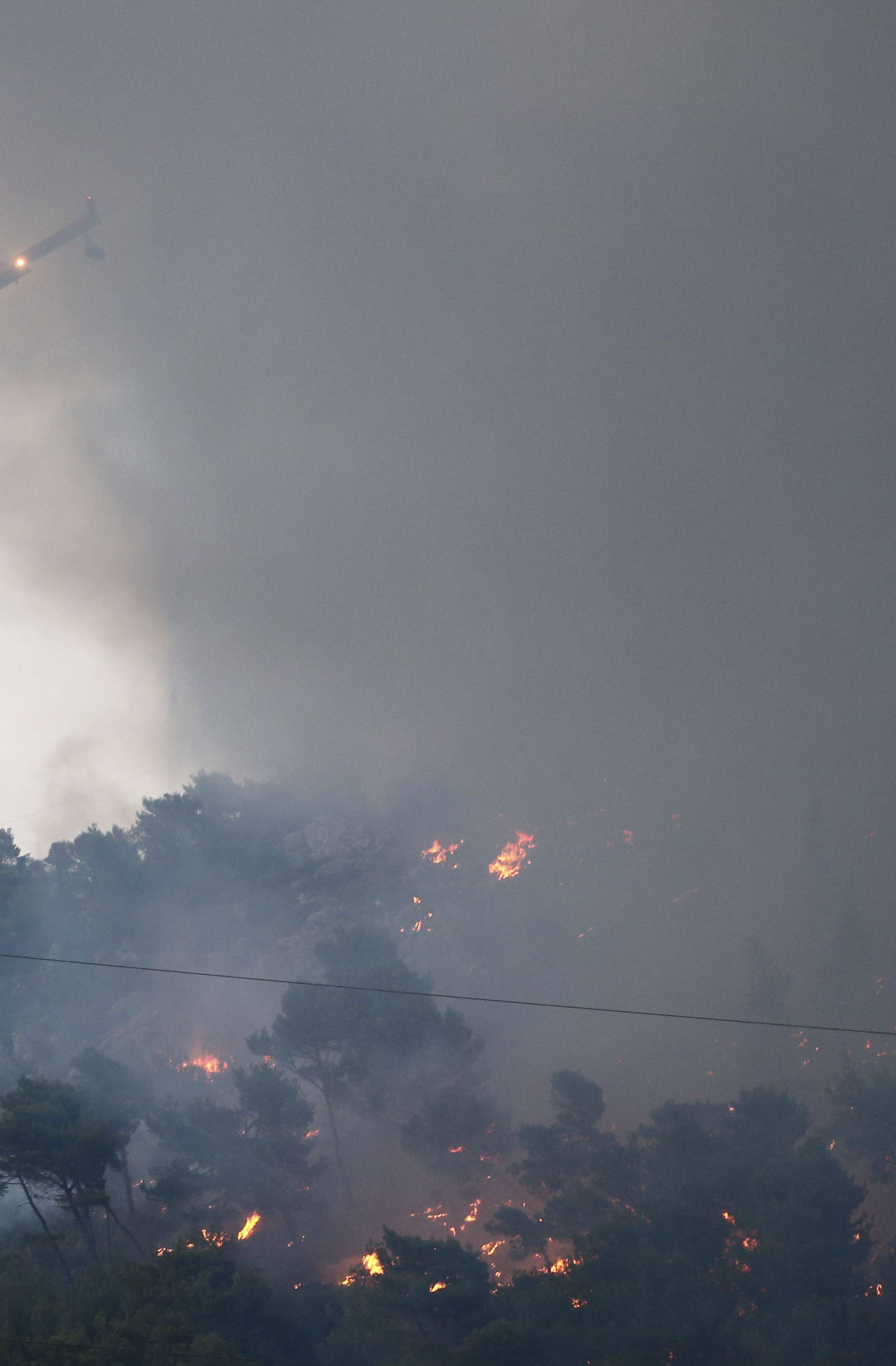 A firefighting plane drops water to extinguish a wildfire in the village of Mravince near Split