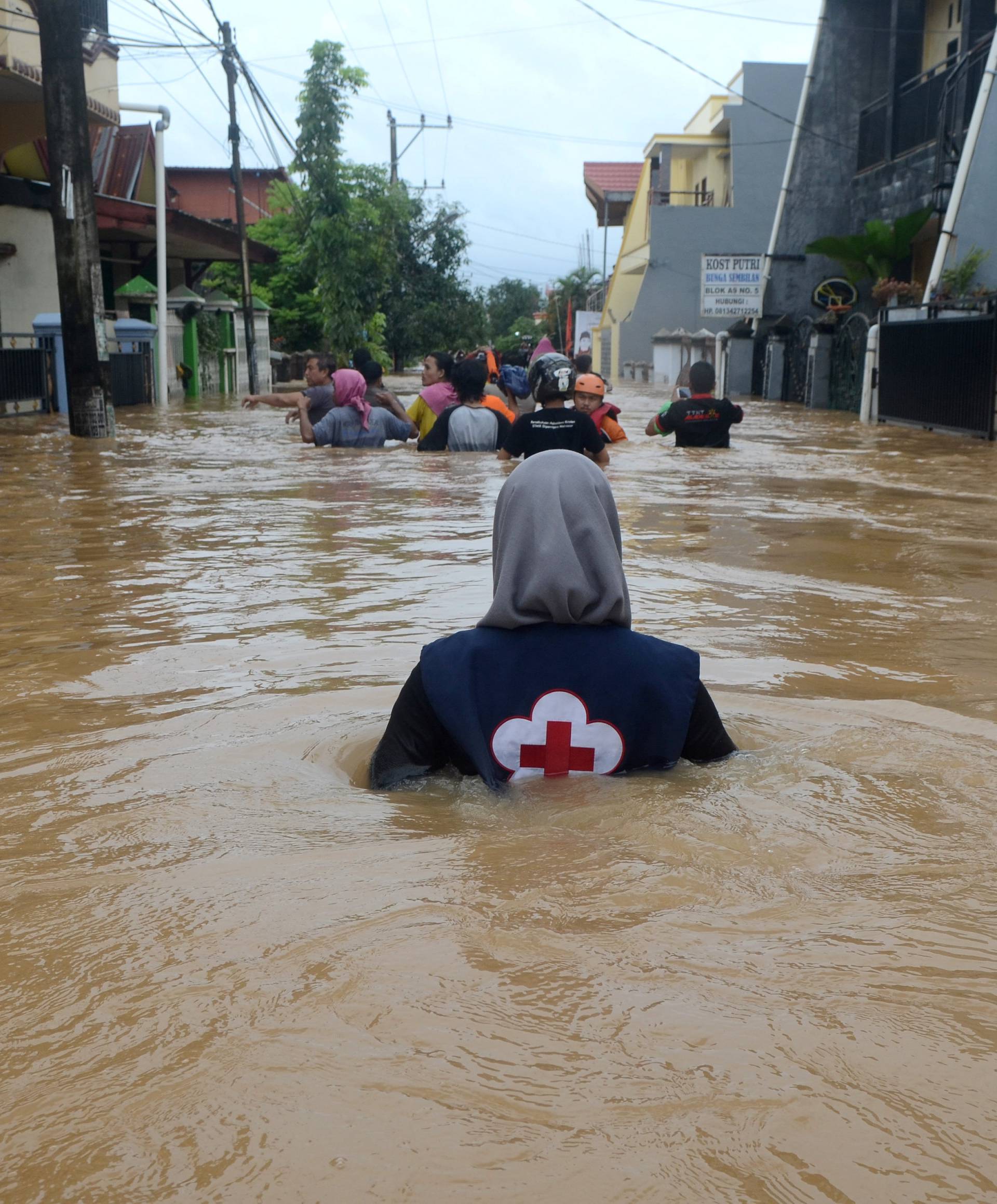 A volunteer wades through floods at a residential area in Makassar