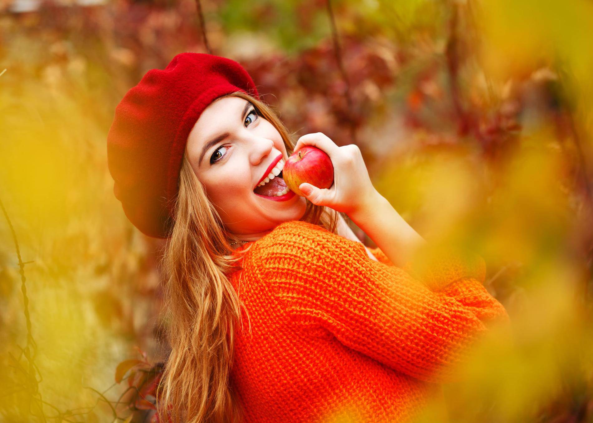 Lovely girl in beret and sweater, holding ripe apple and smiling