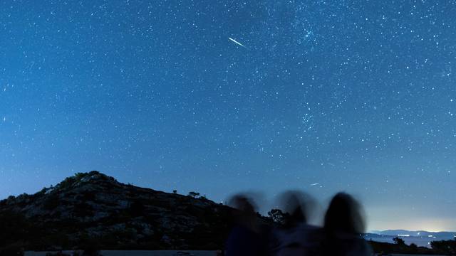 People watch as meteor streaks in the night sky during the annual Perseid meteor shower on the island of Lastovo