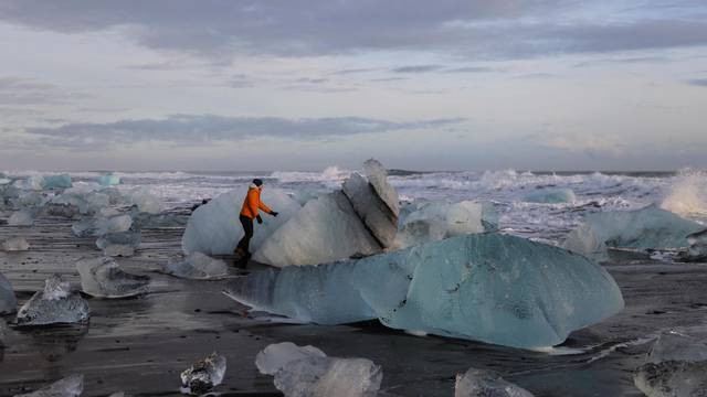 Tourists look at the blocks of ice that have broken off Jokulsarlon glacier lagoon at Diamond beach in Iceland