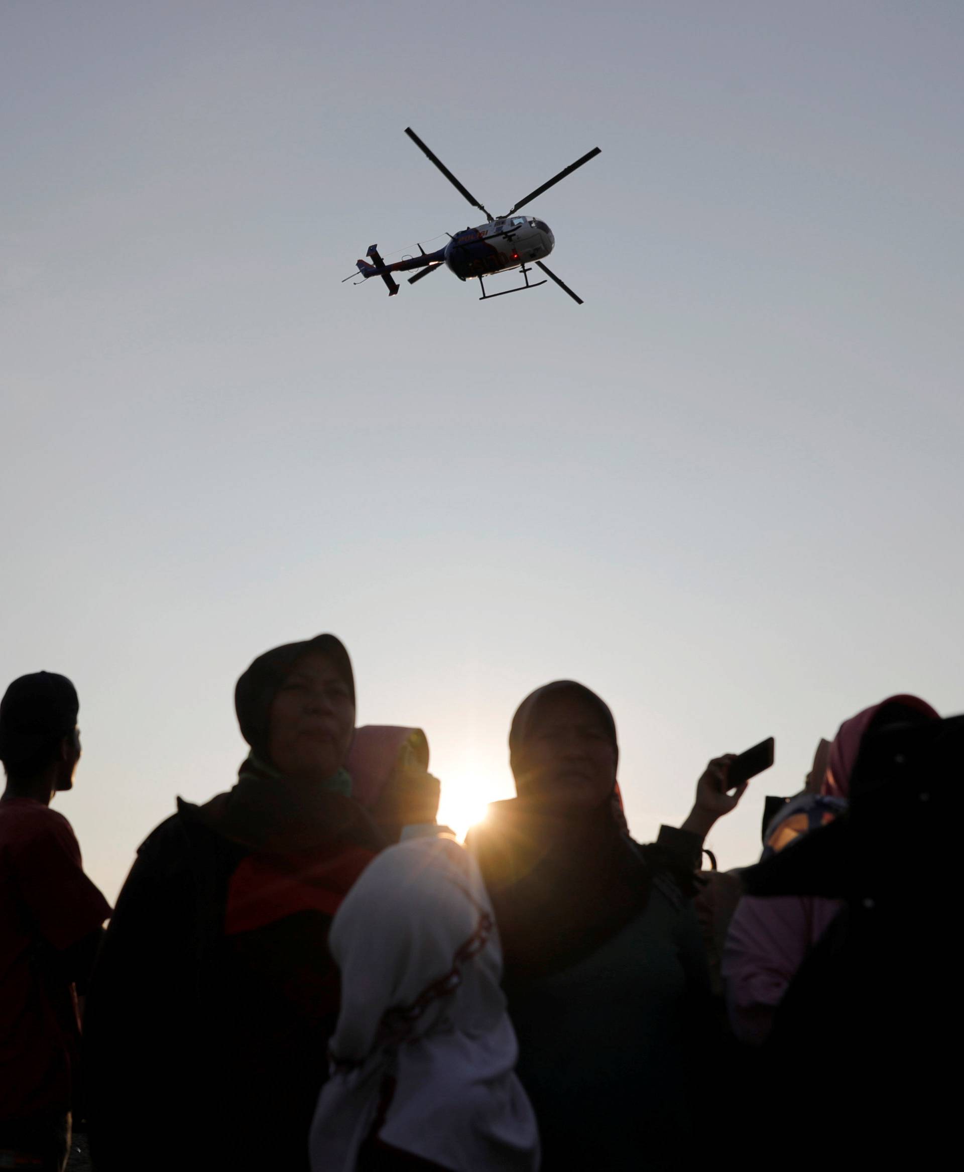People watch a rescue team, as a helicopter flies overhead, to the location of the Lion Air flight JT610 crash site off the coast of Karawang regency