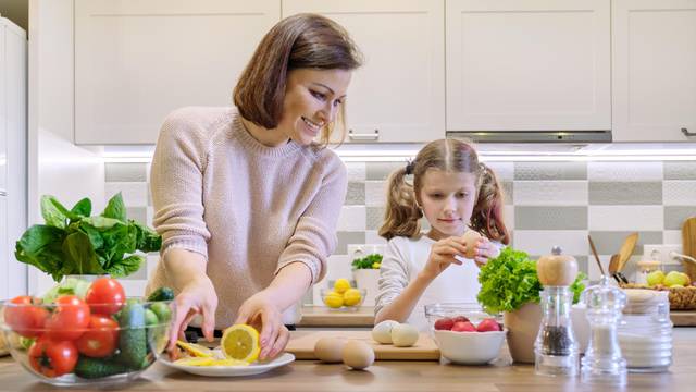 Smiling mother and daughter 8, 9 years old cooking together in kitchen vegetable salad. Healthy home food, communication parent and child.