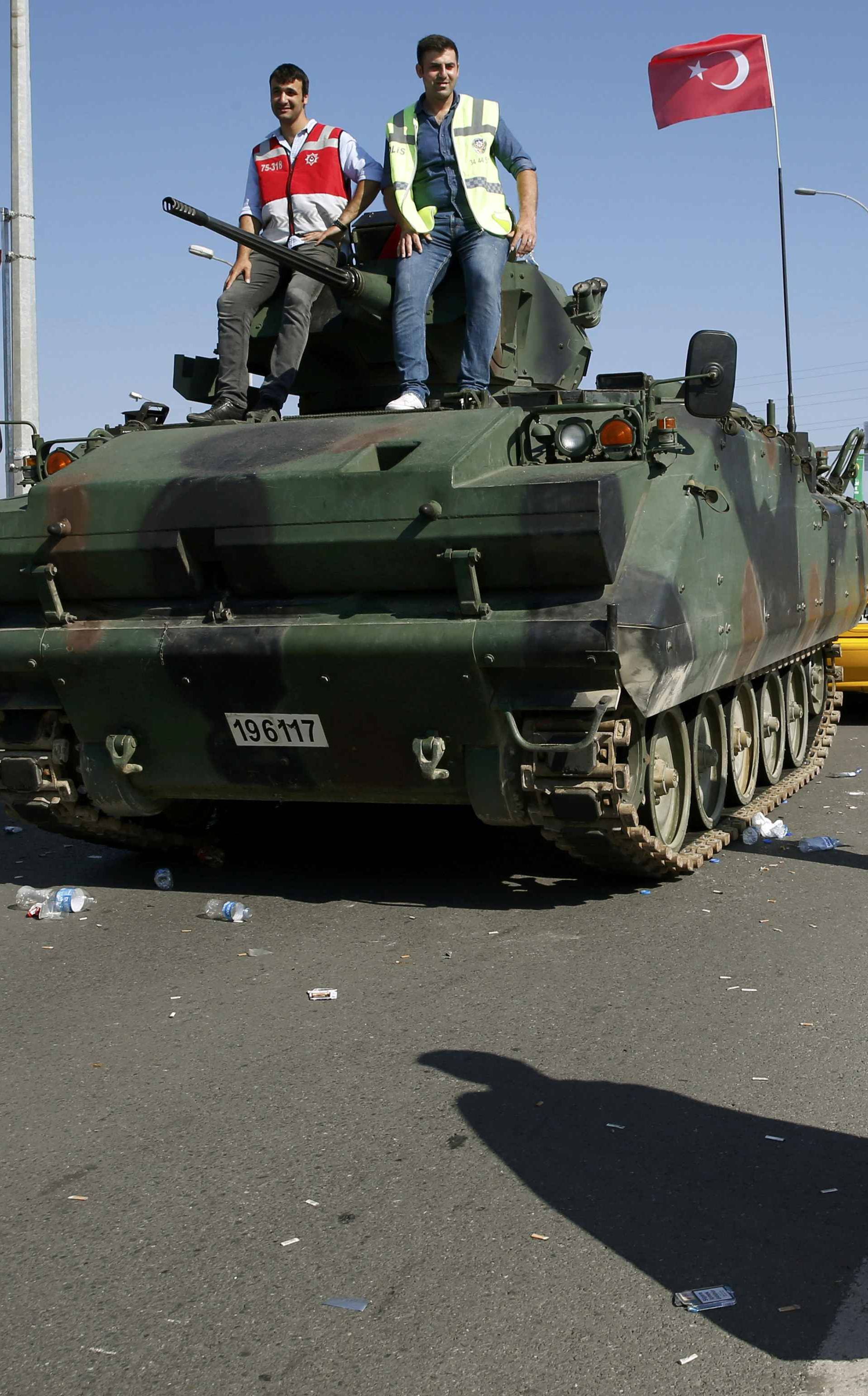 A man wrapped in a Turkish flag walks past a military vehicle in front of Sabiha Airport, in Istanbul