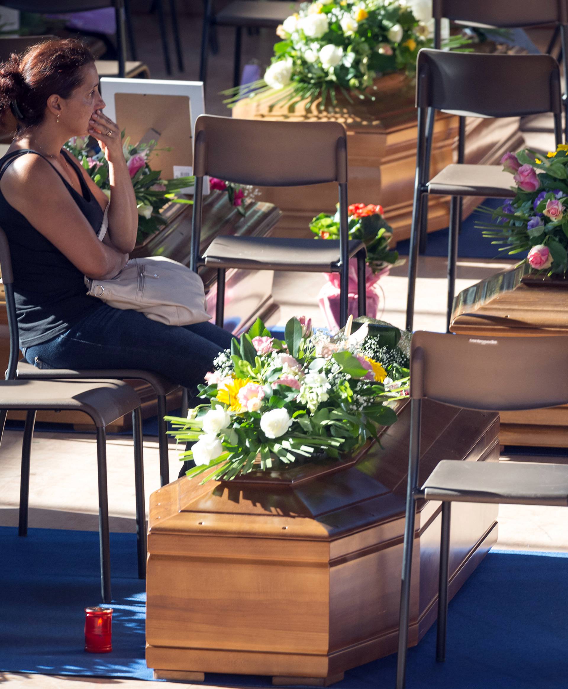 A woman sits next to a coffin to pay her respects as she attends a funeral for the earthquake victims inside a gym in Ascoli Piceno