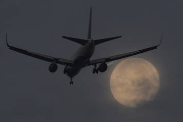 A passenger aircraft makes it's landing approach to Heathrow airport in front of a "super moon" at dawn in west London