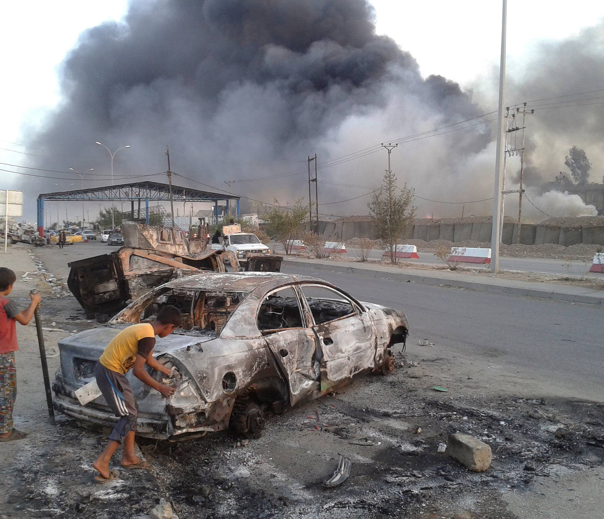Civilian children stand next to a burnt vehicle during clashes between Iraqi security forces and al Qaeda-linked Islamic State in Iraq and the Levant (ISIL) in Mosul