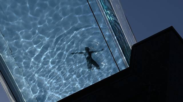 A person relaxes during hot weather at the Embassy Gardens Sky Pool, a transparent acrylic swimming pool suspended between two buildings, in London