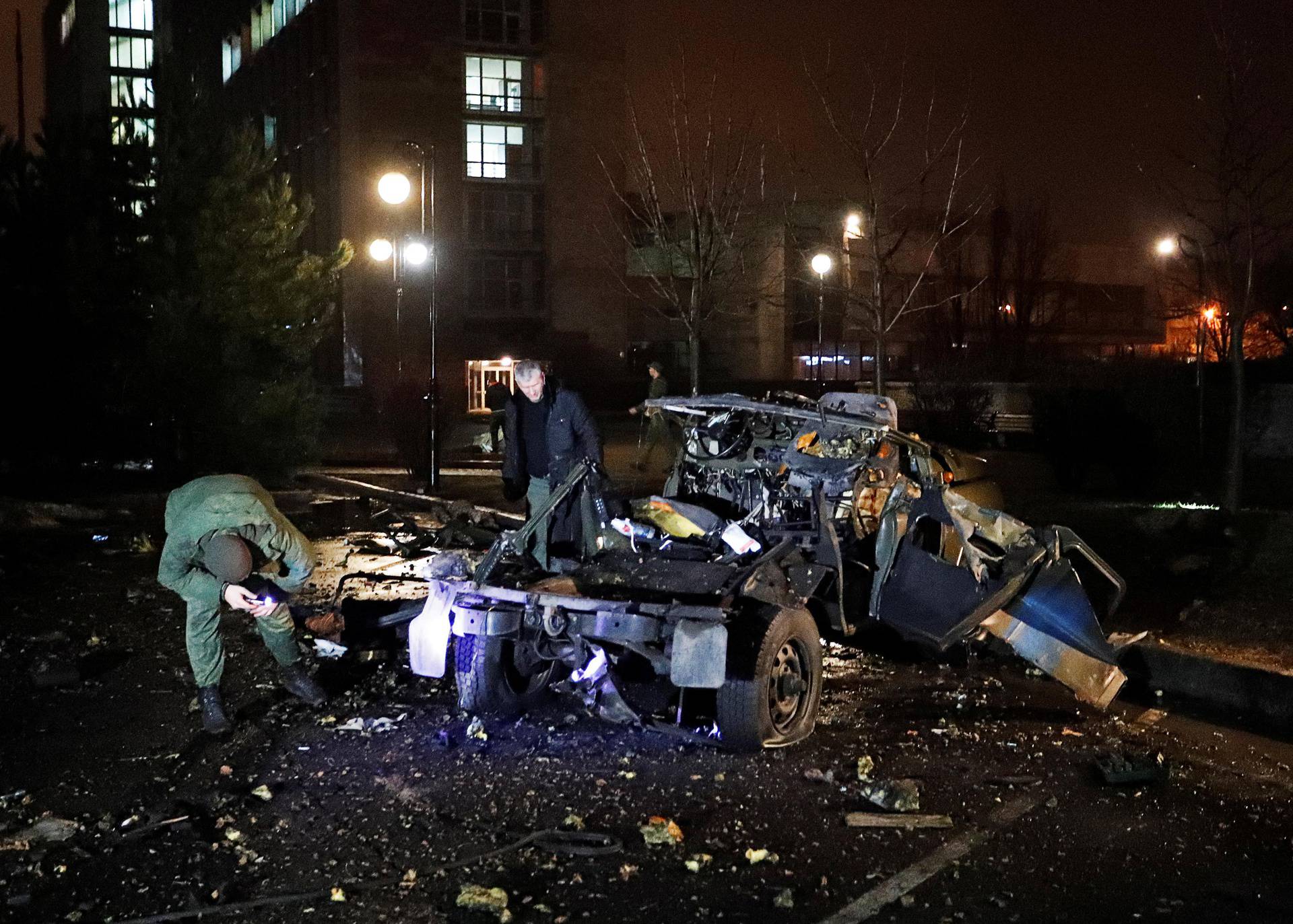 Men inspect a wreckage of a car that according to the local authorities was blown up in Donetsk