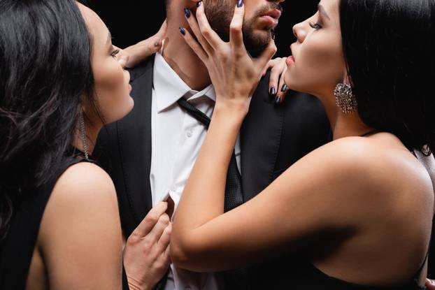 hot, elegant women seducing young man in suit isolated on black