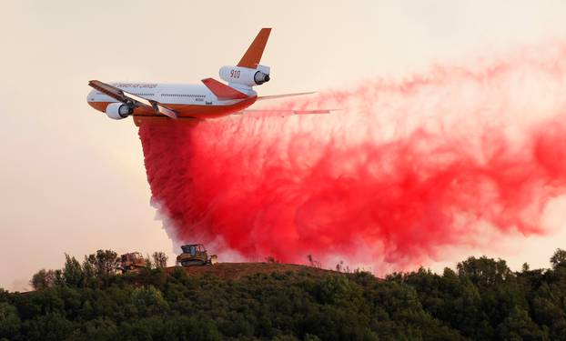 A DC-10 air tanker drops fire retardant along the crest of a hill to protect the two bulldozers below that were cutting fire lines at the River Fire in Lakeport, California