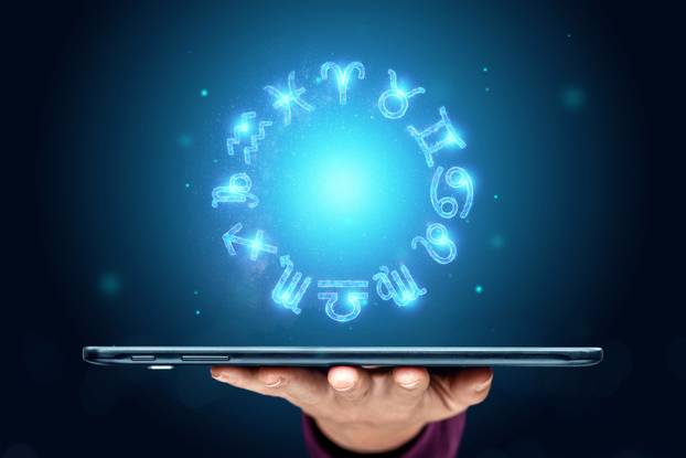 Tablet and hologram 12 zodiac signs, horoscope signs, neon on blue background. The concept of fate, predictions, fortune teller. copy space.