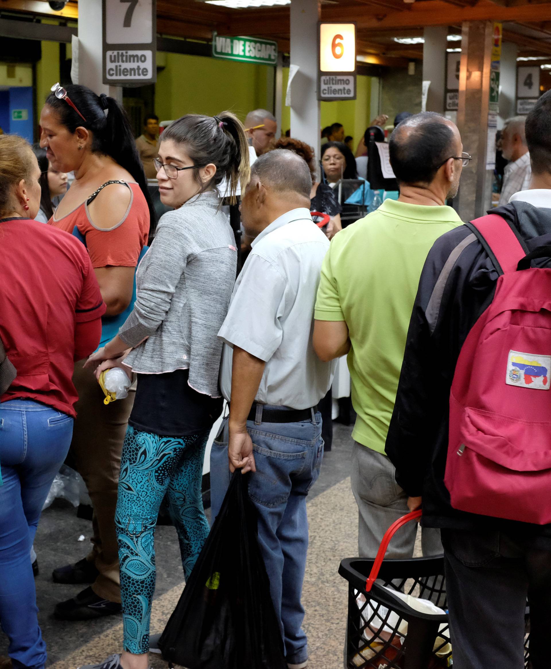 People queue to pay for food at the cashier of a supermarket in downtown Caracas