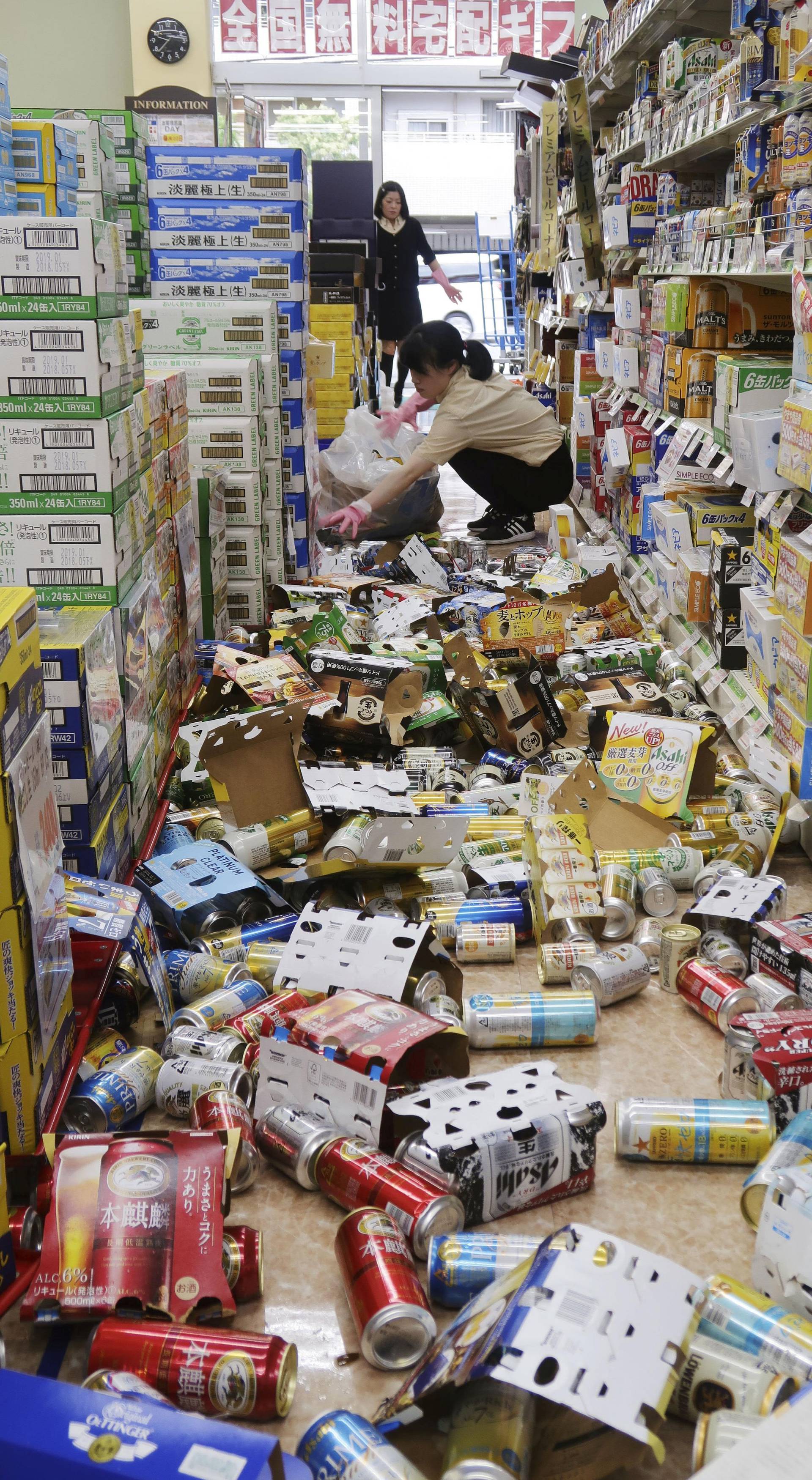 Employees try to remove bottles and cans of beverages which are scattered by an earthquake at a liquor shop in Hirakata